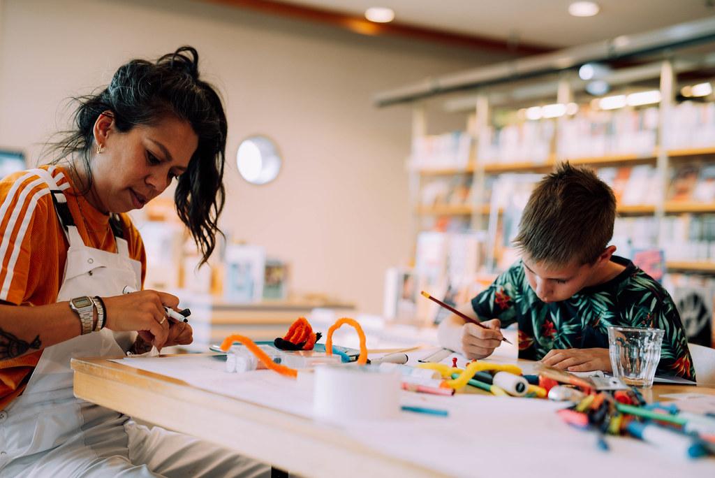 Een kind en volwassene die samen aan het knutselen zijn met stiften, potloden en plaksels
