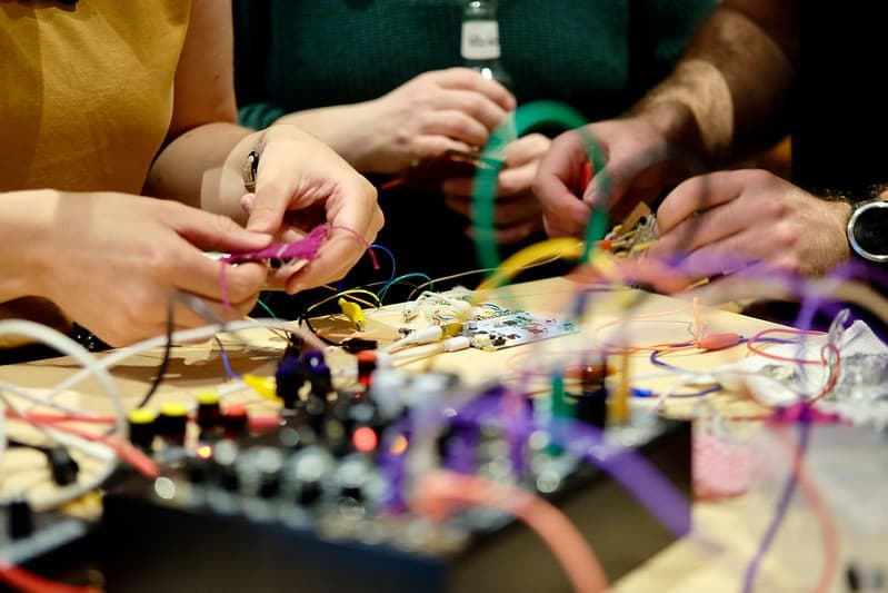 Beeld van electronica en textieldraden, en 3 personen die met hun handen bezig zijn om draad te verbinden