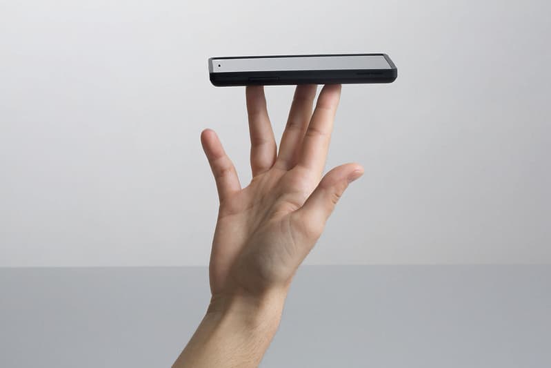 A white hand balances a black smartphone (fairphone) on the top of their fingers