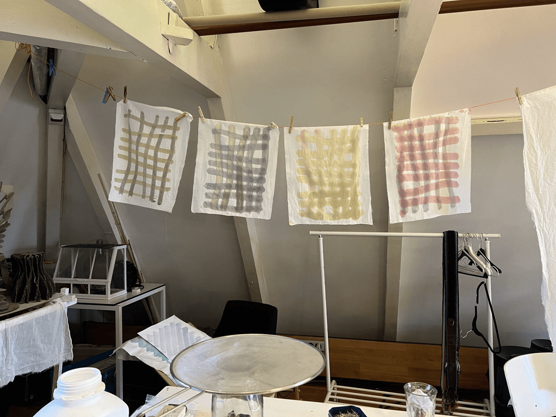 Four white cloths are hanging on a clothes line with several colors printed on them, such as green, yellow and red