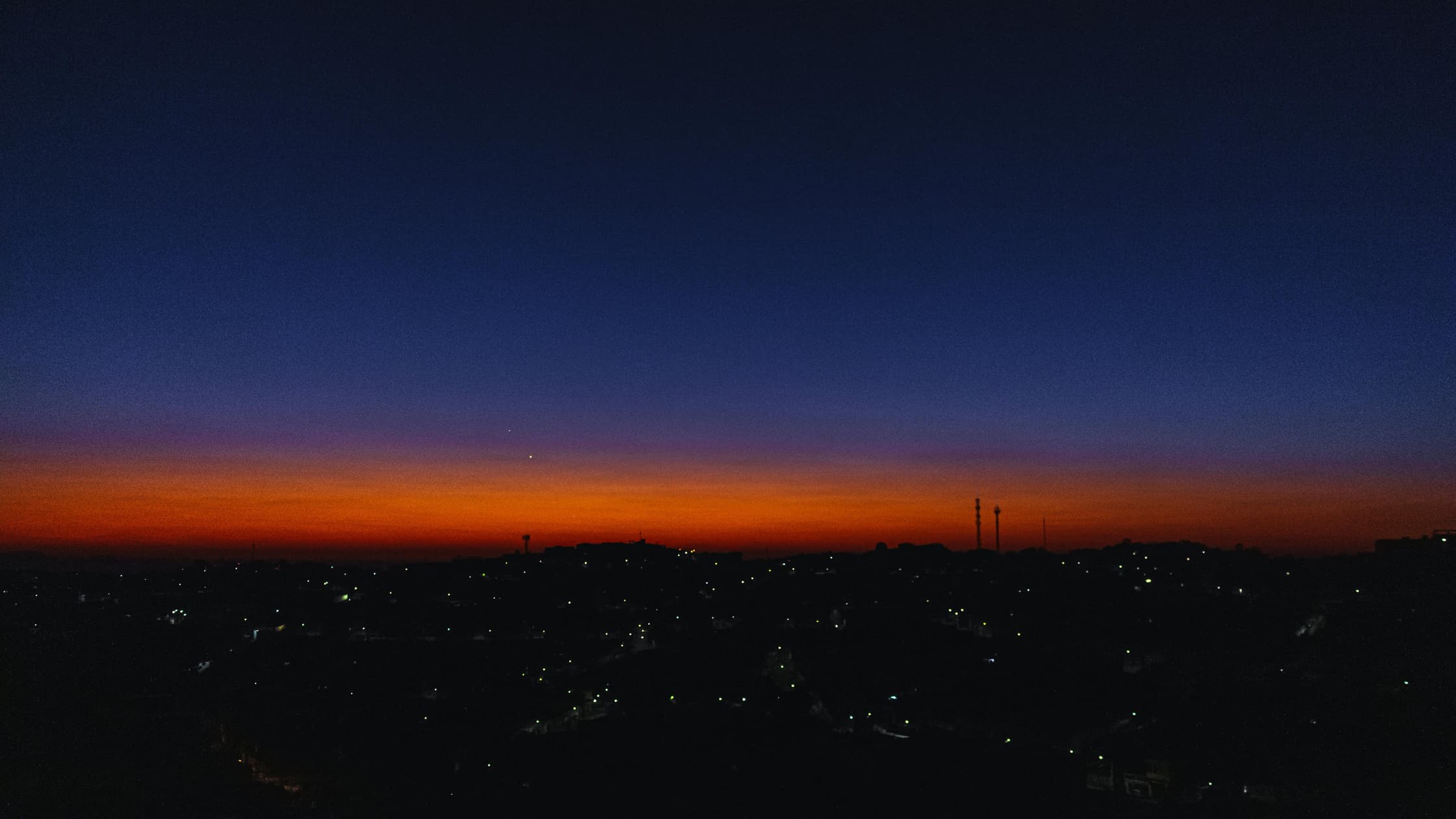 A dark skyline with a faint orange glow and fark blue sky