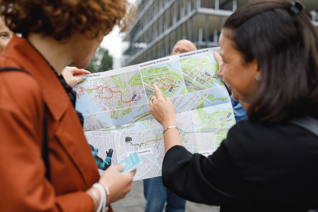 Twee mensen kijken op een gedrukte kaart van Amsterdam. De persoon aan de rechterkant wijst een plek aan op de kaart.
