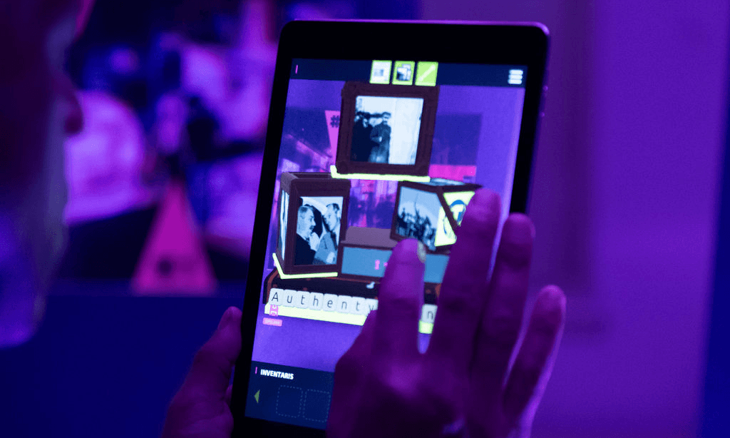 Een persoon kijkt op een tablet en is iets aan het intoetsen op het scherm, De omgeving is donkerpaars verlicht en op het scherm lichten een aantal visuele objecten op.