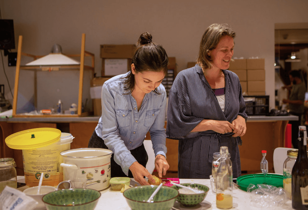 Twee dames staan achter een tafel met potjes, kommetjes, flesjes