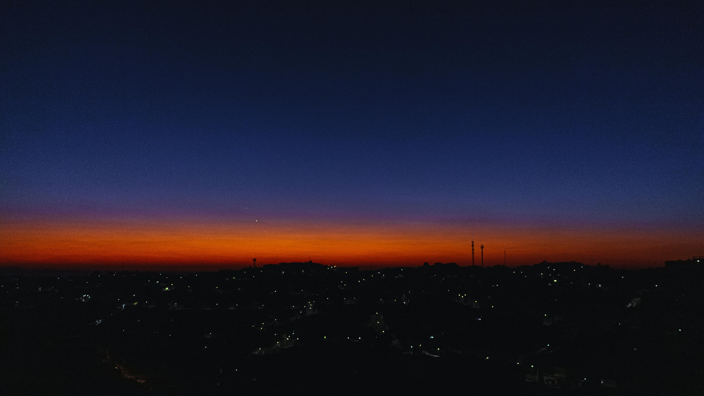 A dark skyline with a faint orange glow and fark blue sky