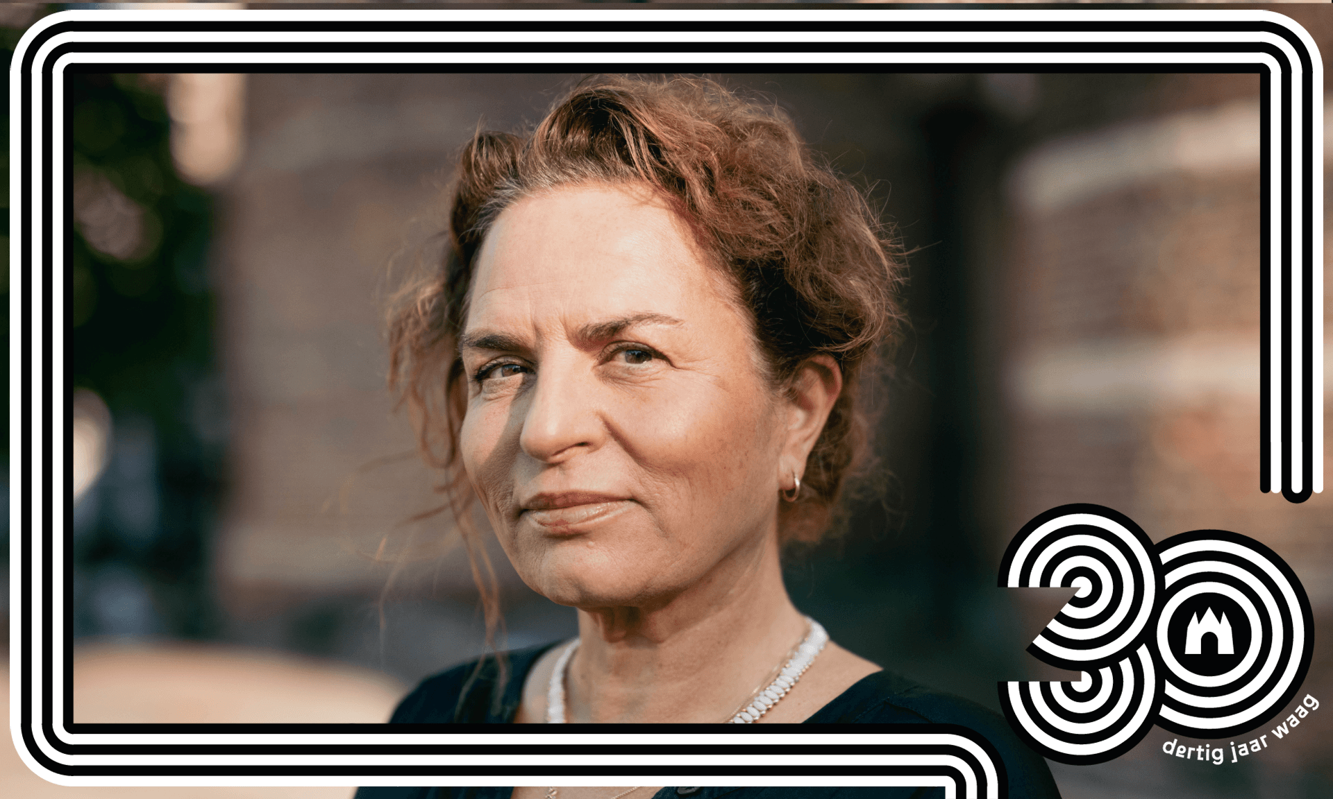 Portretfoto van Marleen Stikker die voor het gebouw van de Waag op de Nieuwmarkt staat.