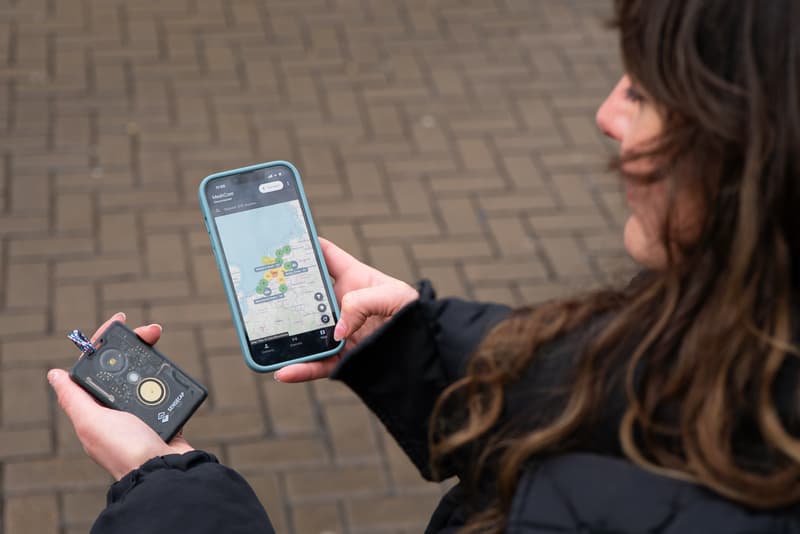 Persoon houdt een meshapparaat en telefoon met kaart van meshgebruikers vast.