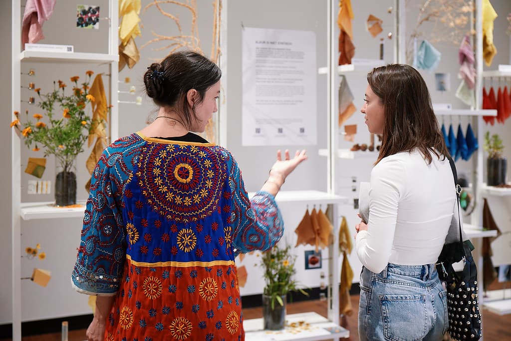Two visitors view the chromatic relations expo, they are surrounded by textiles in colorful dyes