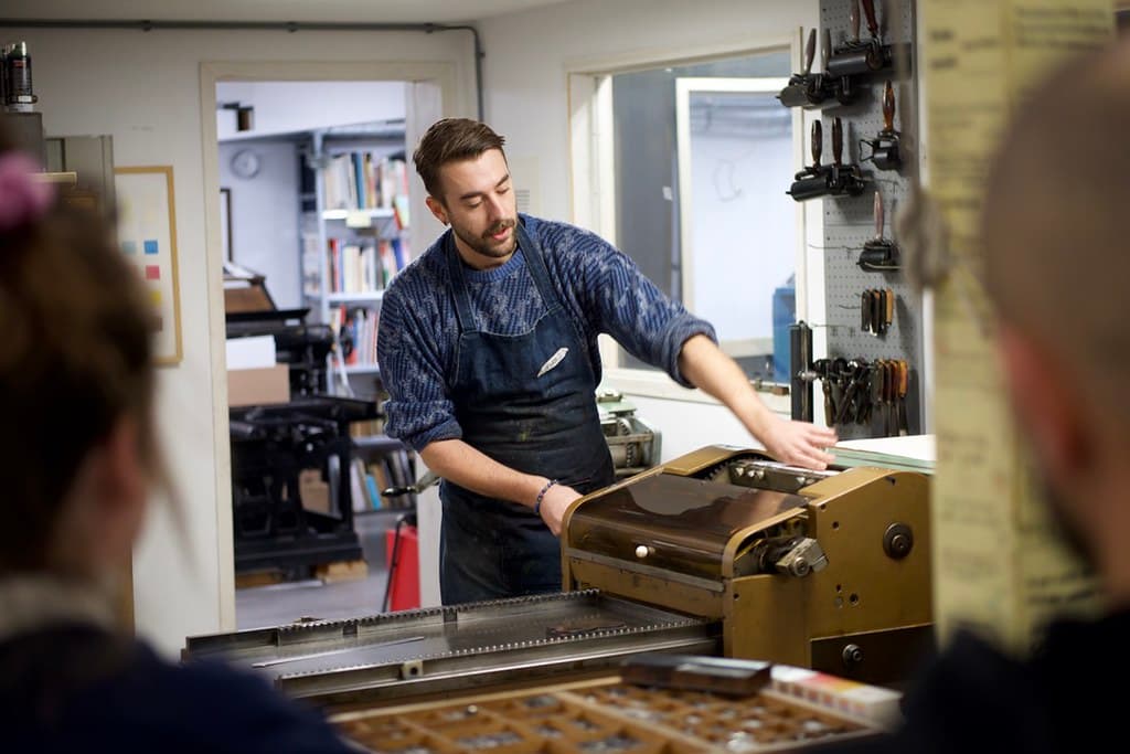 Een man die een schort draagt staat bij een machine en geeft uitleg.