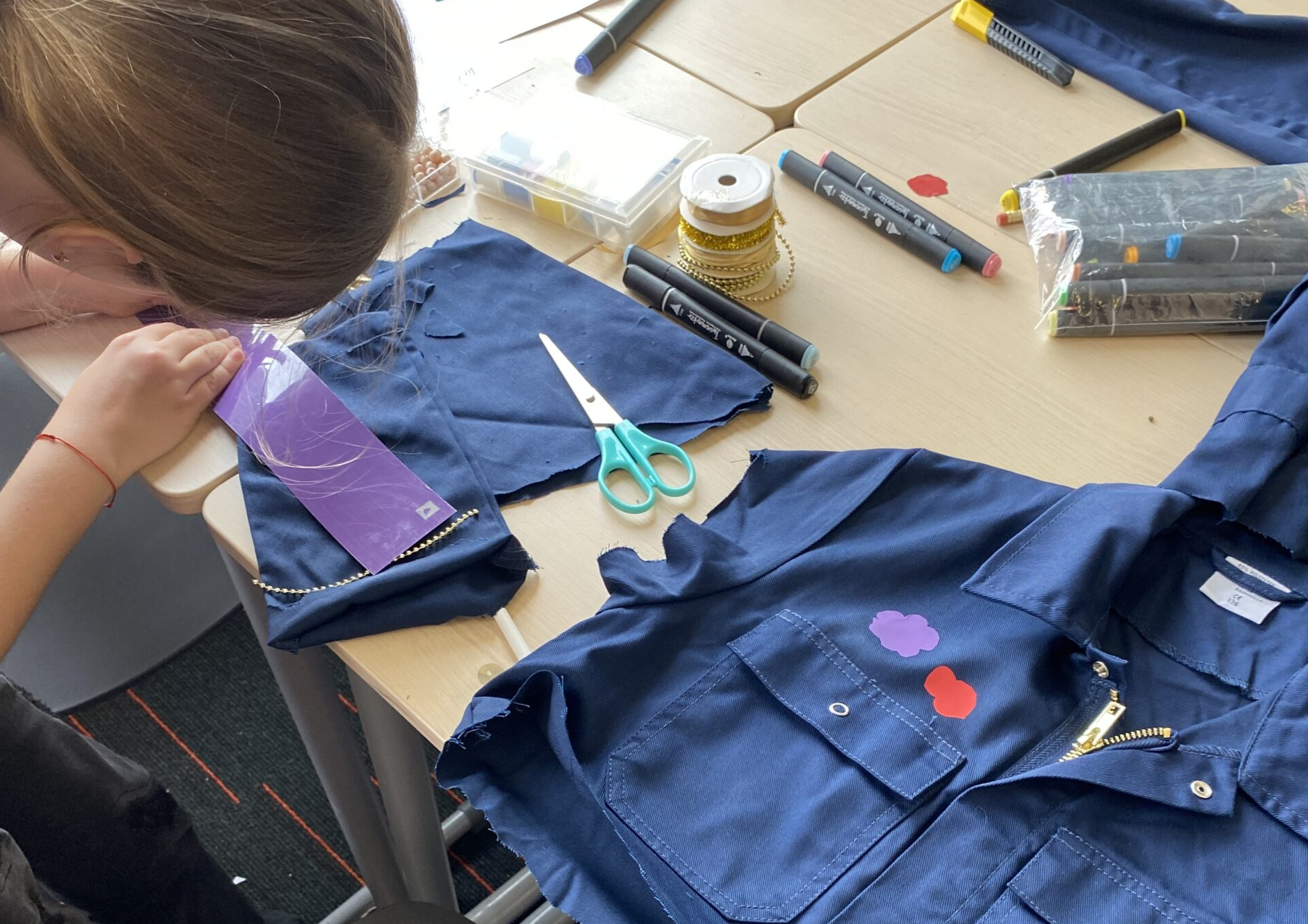 A participant is working on a blue overall by adding pieces of cloth