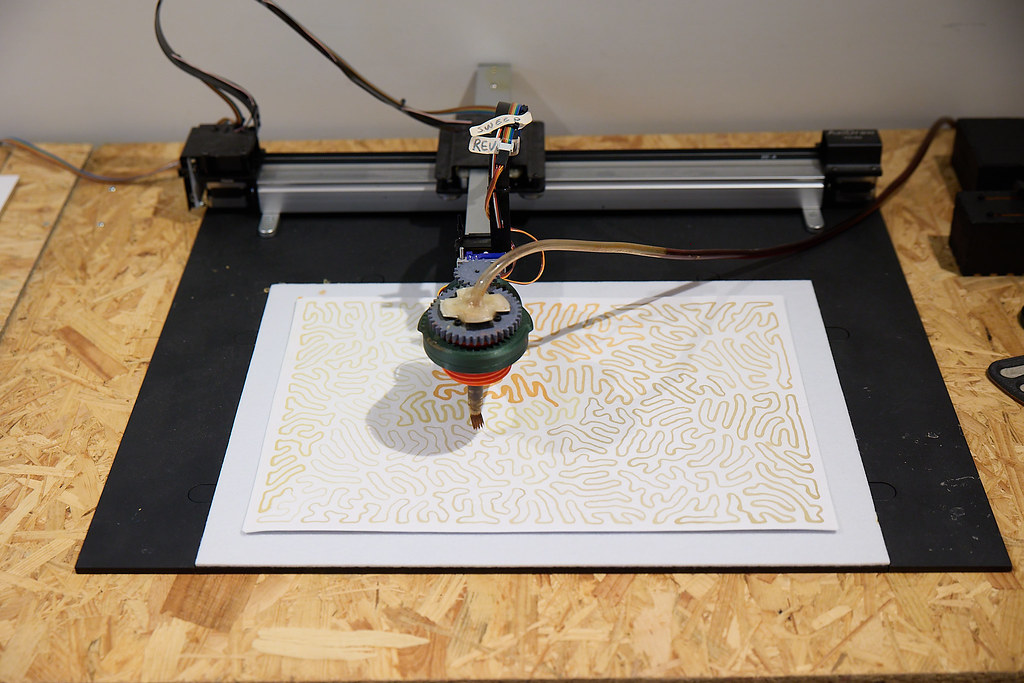 Close-up of the HaptiColor Machine in action, printing wavy patterns of yellow dye on a whit canvas